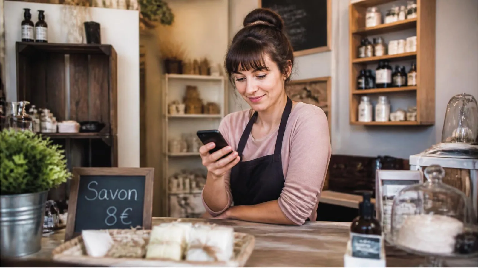 Une commerçante consulte son téléphone à son comptoir.