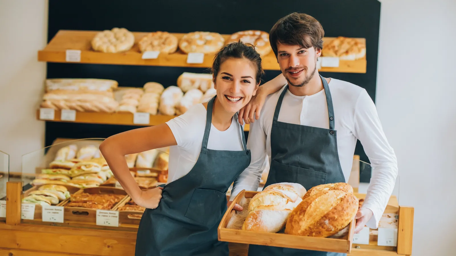 Deux boulangers souriants dans leur boutique, devant leur présentoir à pains.